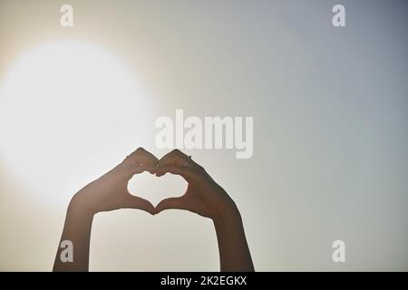 Liebe ohne Grenzen. Eine kurze Aufnahme einer Frau, die mit ihren Händen gegen einen blauen Himmel eine Herzform formt. Stockfoto