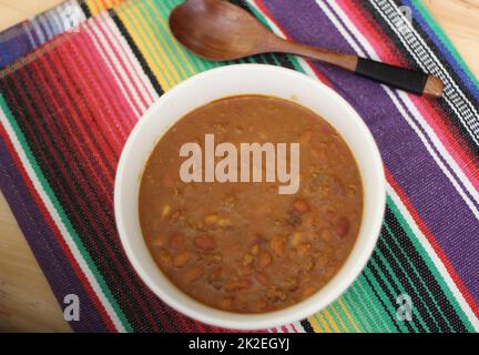 Schüssel Chili mit Pintobohnen auf dem Tisch mit Paprika und trockenen Bohnen im Hintergrund Stockfoto