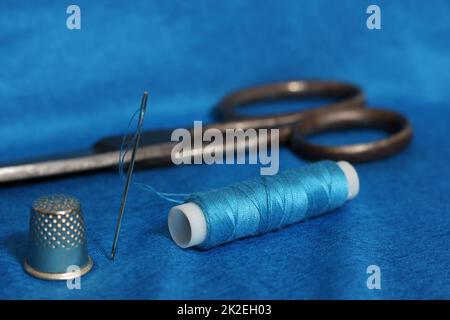 Spule aus blauem Faden, Nimble und Nadel auf blauem Stoff Stockfoto