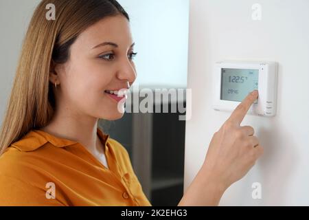 Nahaufnahme einer jungen Frau, die die Temperatur der Zentralheizung zu Hause am Thermostat anpasst. Senken Sie die Temperatur, um Energie zu sparen. Stockfoto