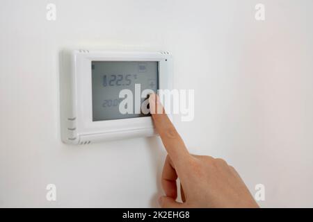 Senken der Temperatur zur Energieeinsparung. Digitaler Thermostat für die Zentralheizung mit menschlicher Hand zu Hause. Stockfoto