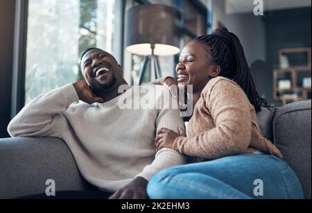 Wir gehen nie einen Tag ohne zu lachen. Eine kurze Aufnahme eines glücklichen jungen Paares, das zusammen sitzt und sich während ihres Wochenendes zu Hause verbindet. Stockfoto