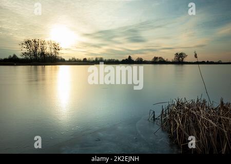 Wunderschöner Sonnenuntergang über einem gefrorenen See mit Schilf Stockfoto