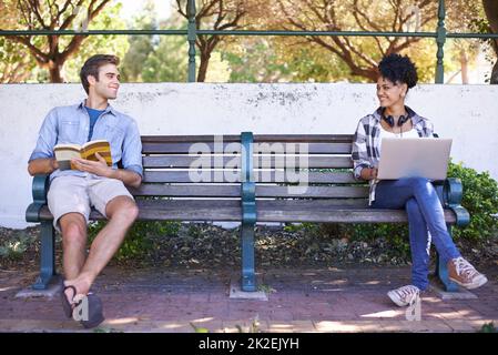 Einander zum ersten Mal wahrzunehmen. Zwei Schüler sitzen auf gegenüberliegenden Seiten einer Bank mit ihrem Lesematerial vor ihnen und schauen einander an. Stockfoto