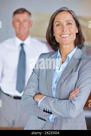 Selbstbewusst und erfolgreich. Porträt einer reifen Geschäftsfrau mit ihrem Kollegen im Hintergrund. Stockfoto