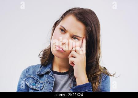 Dein Kopf kann dein schlimmster Feind sein. Studioaufnahme einer jungen Frau, die vor grauem Hintergrund nachdenklich aussieht. Stockfoto