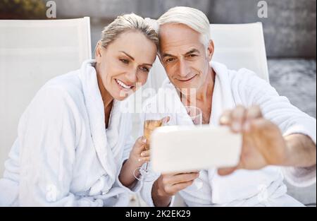 Ein paar besondere Erinnerungen machen. Aufnahme eines fröhlichen Paares mittleren Alters, das ein Selbstporträt zusammen macht, während er tagsüber ein Glas Champagner im Spa genießt. Stockfoto