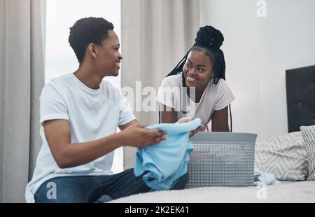 Die Aufteilung der Aufgaben entlastet die Arbeit. Aufnahme eines jungen Paares, das zu Hause gemeinsam Wäsche waschen soll. Stockfoto