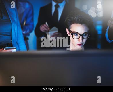 Ich arbeite unter Druck gut. Ausgeschnittene Aufnahme einer jungen Frau, die spät arbeitet und Kollegen im Hintergrund stehen. Stockfoto