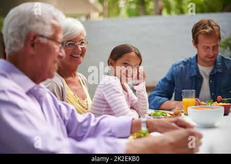 Unterhaltsames Familienessen. Aufnahme einer glücklichen, generationsübergreifenden Familie, die draußen zusammen zu Abend gegessen hat. Stockfoto