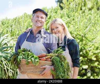 Stolz auf ihre Produkte. Ein reifes Bauernpaar hält einen Korb mit frisch gepflücktem Gemüse. Stockfoto