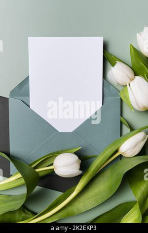 Mockup Papier Blankin Umschlag Einladung oder Grußkarte und weißen Tulpen. Stockfoto