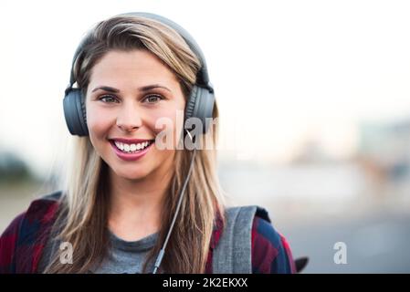 Jamming weg in der Stadt. Porträt einer attraktiven jungen Frau, die Kopfhörer trägt, während sie durch die Stadt geht. Stockfoto