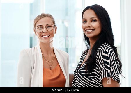 Waren hier, um Ihnen zu helfen. Beschnittenes Porträt von zwei attraktiven jungen Geschäftsfrauen, die in ihrem Büro stehen. Stockfoto