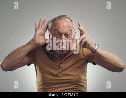 Int auch mit meinem inneren Kind. Studioaufnahme eines älteren Mannes, der vor grauem Hintergrund ein lustiges Gesicht macht. Stockfoto