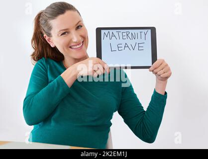 Shes erwartet ihr Baby bald. Aufnahme einer Schwangeren, die ein Tablet mit den Worten Mutterschaftsurlaub auf dem Bildschirm hochhält. Stockfoto