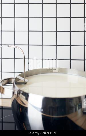 Der Prozess der Herstellung von Joghurt. Die Milch wird durch Bakterien erhitzt und fermentiert. Milch in einem Topf auf dem Herd. Vertikales Foto. Stockfoto