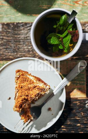 Ein großes Stück Kuchen auf Honigkuchen mit einem Becher schwarzen Tees mit Zitrone und Minze. Vertikales Foto. Stockfoto