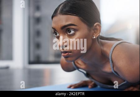 Gewinner verlieren nie den Fokus. Nahaufnahme einer attraktiven jungen Frau, die zu Hause auf ihrer Sportmatte trainiert. Stockfoto