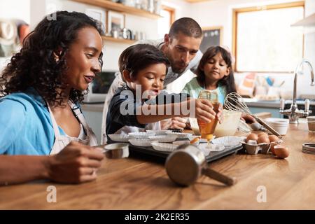 Ich möchte etwas mehr Honig in meinem. Eine kleine Aufnahme eines jungen Paares, das mit seinen beiden Kindern zu Hause backt. Stockfoto