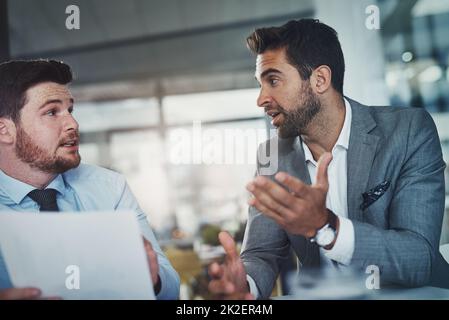 Die Zahlen zum Einsatz bringen. Aufnahme von zwei jungen Geschäftsleuten, die gemeinsam in einem modernen Büro Papierkram durchmachen. Stockfoto