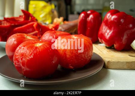 Gebrühte Tomaten, geschält auf einem Teller, Paprika auf einem Holzbrett Stockfoto