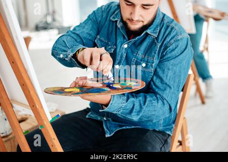 Man kann nie genug Blau haben. Eine kleine Aufnahme eines hübschen jungen Künstlers, der während einer Kunstklasse im Studio Farbe auf eine Palette drückt. Stockfoto