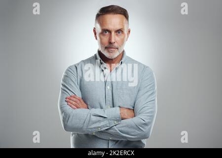 Ich habe keine Zeit, mich umzusehen. Studioporträt eines reifen Mannes, der mit gefalteten Armen vor grauem Hintergrund steht. Stockfoto