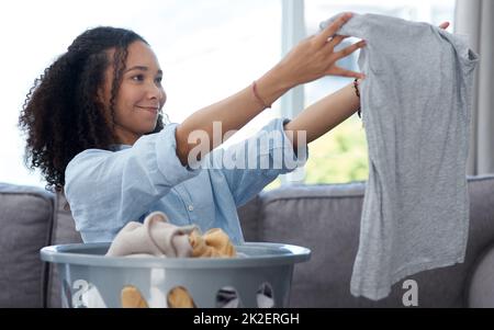 Das Waschmittel hat wirklich alle Flecken herausbekommen. Aufnahme einer jungen Frau, die ihre frisch gereinigte Wäsche zu Hause zusammenfaltete. Stockfoto