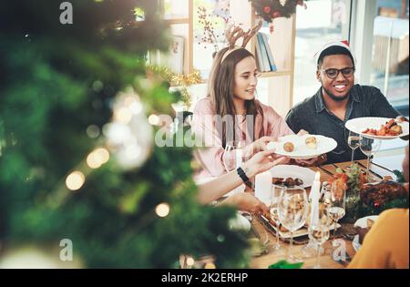 Der Moment, auf den sie gewartet haben Eine kurze Aufnahme einer Gruppe von fröhlichen jungen Freunden, die zu Hause gemeinsam zu Weihnachten essen. Stockfoto