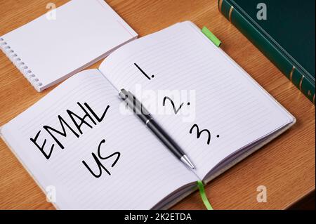 Inspiration mit Schild E-Mail uns. Business Showcase Senden einer Werbebotschaft an eine Gruppe von Shows mithilfe von Mail Blank Open Notizbüchern mit Stiftstapel Container Over Table. Stockfoto