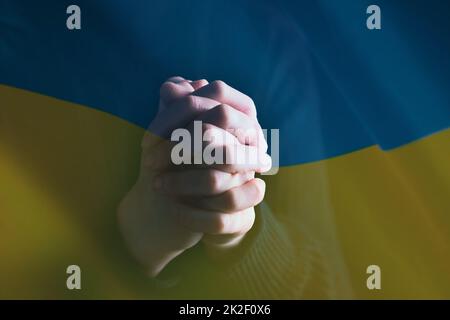 Nahaufnahme der ukrainischen Flagge mit betenden Händen Stockfoto