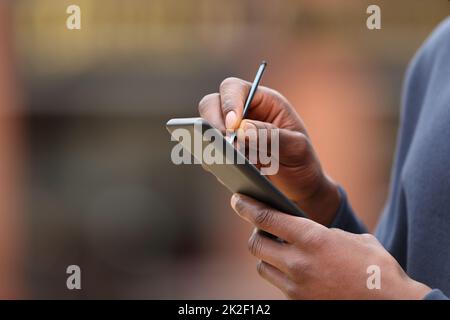 Ein Mann mit schwarzen Händen, der einen Stift am Telefon benutzt Stockfoto