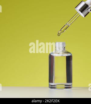 Ätherisches Öl, das aus dem bernsteinfarbenen Glasbehälter fällt. Weiße Flasche kosmetisches Öl mit Pipette, grüner Hintergrund Stockfoto