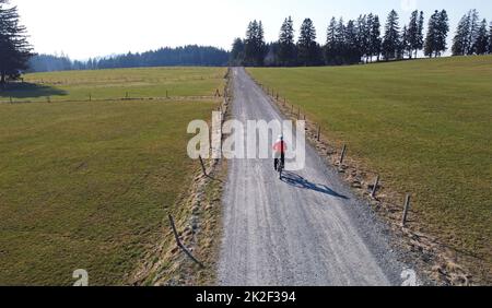 Drohnenaufnahme einer Radfahrerin auf einsamer Straße mit Schatten Stockfoto