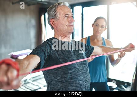 Aufrechterhaltung gesunder Muskeln, egal wie alt sie sind. Aufnahme eines älteren Mannes, der mit Hilfe eines Physiotherapeuten Widerstandsbänder verwendete. Stockfoto