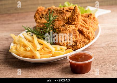 Gebratenes Huhn und Kartoffelchip mit Rosmarinblatt, kalorienreiche Junk-Food auf weißem Teller serviert Stockfoto