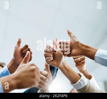 Wir lieben das, was Sie tun. Aufnahme einer Gruppe von nicht erkennbaren Geschäftsleuten, die in einem Büro den Daumen nach oben zeigen. Stockfoto