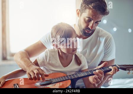 Zeigt ihr, wie sie ihre Gefühle durch Musik ausdrücken kann. Aufnahme eines kleinen Mädchens, das mit ihrem Vater Gitarre spielt. Stockfoto