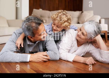 Spaß auf dem Boden mit Oma und Gramps. Ein kleiner Junge, der auf dem Boden seines Wohnzimmers auf seinen Großeltern liegt. Stockfoto