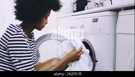 Schön und frisch. Aufnahme einer fokussierten jungen Frau, die tagsüber Kleidung in die Waschmaschine legt, um sich zu Hause waschen zu lassen. Stockfoto