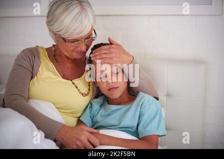 Oma kümmert sich um Sie. Aufnahme einer fürsorglichen Großmutter, die sich zu Hause um ihren kranken Enkel kümmert. Stockfoto