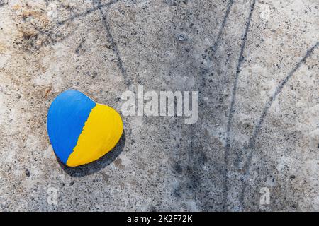 Stein in Herzform, mit ukrainischer Flagge bemalt, liegt auf dem Boden, Beton Stockfoto