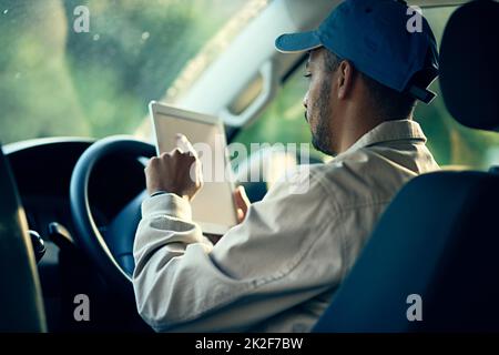 Protokollierung seiner nächsten Lieferung. Ausgeschnittene Aufnahme eines Lieferers, der ein digitales Tablet benutzt, während er in seinem Van sitzt. Stockfoto