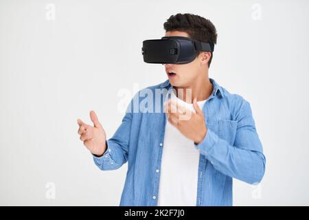 Flucht in den Cyberspace. Studio-Aufnahme eines jungen Mannes, der erstaunt aussagt, während er ein VR-Headset vor weißem Hintergrund trägt. Stockfoto