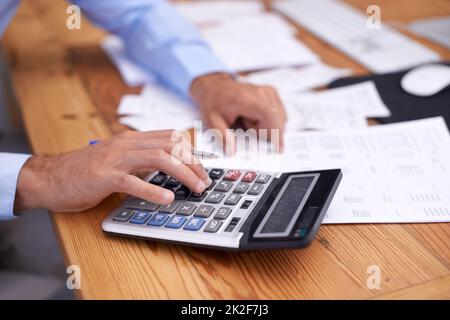 Überprüfen Sie die Zahlen. Ausgeschnittene Aufnahme eines Geschäftsmanns, der in seinem Büro einen Rechner benutzt. Stockfoto