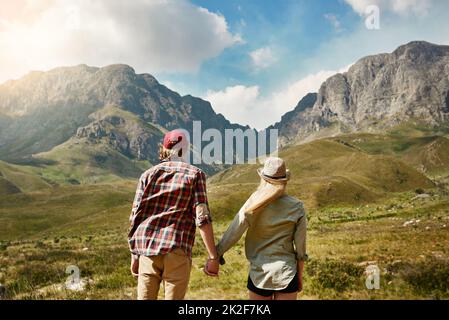 Als Paar neue Höhen erreichen. Rückansicht eines jungen Paares, das einen Bergblick in der Natur bewundert. Stockfoto