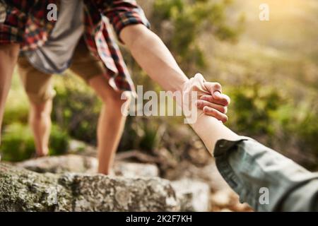 Allein klettern wir auf Felsen, gemeinsam besteigen wir Berge. Eine kurze Aufnahme von Wanderern, die sich gegenseitig beim Aufstieg auf einen Felsen in der Natur helfen. Stockfoto