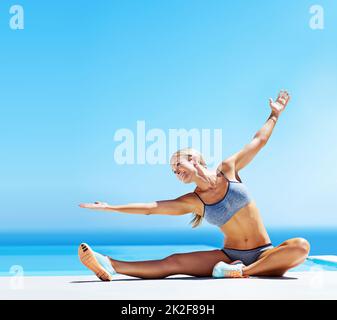 Ihre Fitnessziele zu erreichen. Aufnahme einer jungen Frau, die unter blauem Himmel auf einer Terrasse arbeitet. Stockfoto