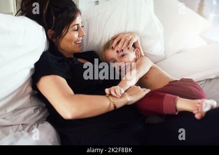 Mein kostbarer kleiner Liebling. Aufnahme eines fröhlichen kleinen Jungen und seiner Mutter, die sich tagsüber auf dem Bett zu Hause entspannen. Stockfoto